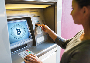 finance, cryptocurrency and technology concept - close up of woman hand inserting bank card to atm machine with bitcoin icon on screen
