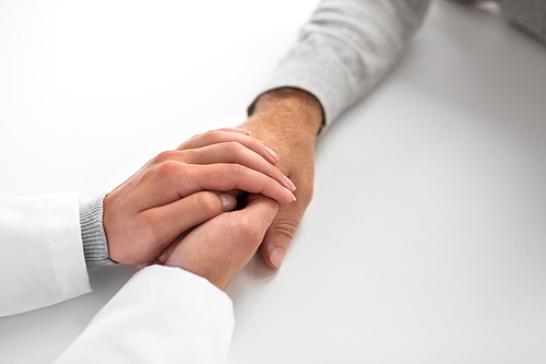 medicine, healthcare and old age concept - close up of young doctor holding senior patient hand