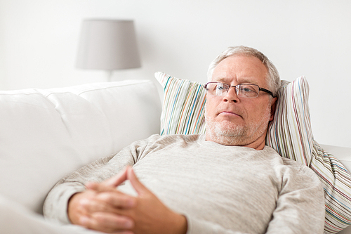 old age, problem and people concept - senior man  lying on sofa and thinking at home