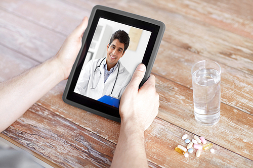 medicine, technology and healthcare concept - close up of patient with pills and water on table having video chat with doctor on tablet pc computer