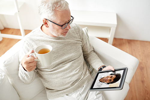 technology, people and communication concept - senior man having video call with partner or customer service operator on tablet pc computer and drinking tea at home