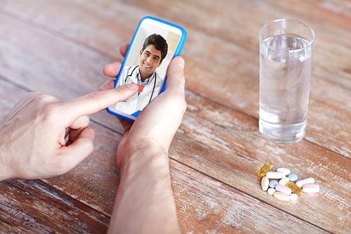 medicine, technology and healthcare concept - close up of patient with pills and water on table having video chat with doctor on smartphone