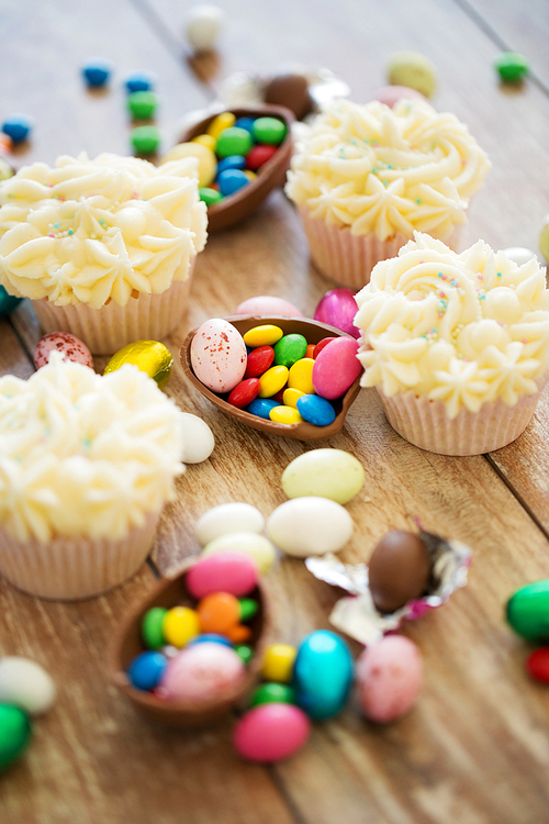 easter, food and holidays concept - frosted cupcakes with chocolate eggs and candies on table