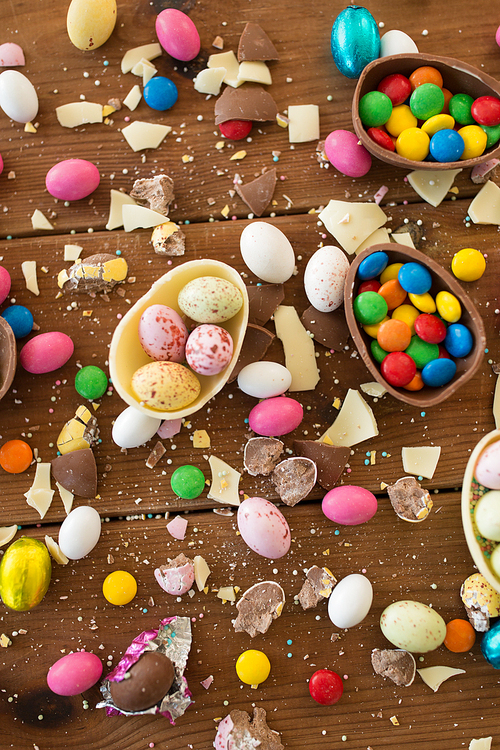 easter, sweets and confectionery concept - chocolate eggs and candy drops on wooden table