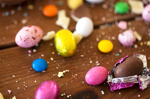 easter, sweets and confectionery concept - close up of chocolate eggs and candy drops on wooden table