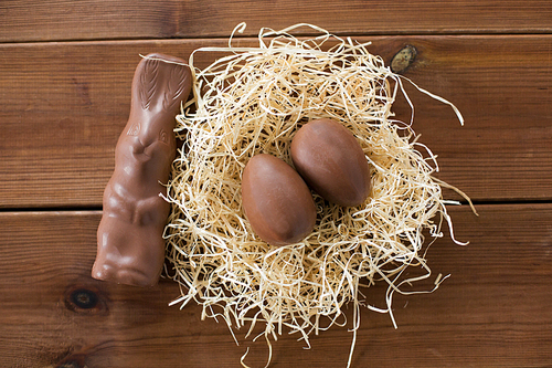 easter, confectionery and holidays concept - chocolate bunny and eggs in straw nest on wooden background