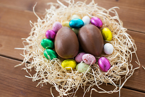 easter, confectionery and holidays concept - close up of chocolate eggs and candies in straw nest on wooden table