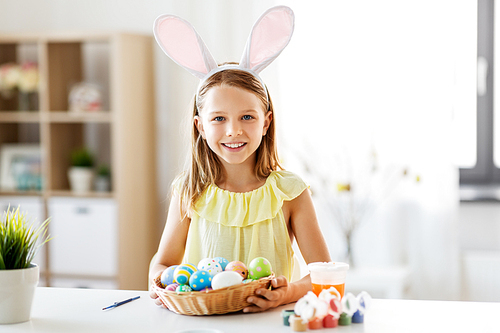 easter, holidays and people concept - happy girl wearing bunny ears headband with colored eggs at home