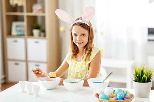 easter, holidays and people concept - happy girl wearing bunny ears headband coloring eggs by liquid dye at home