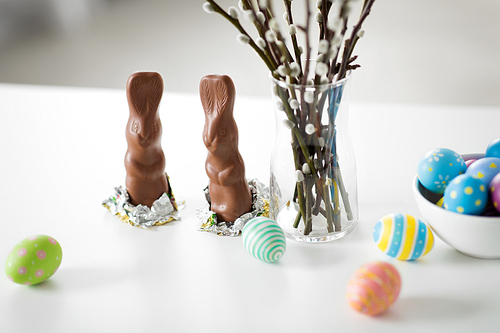 easter, holidays and object concept - close up of pussy willow branches, colored eggs and chocolate bunnies on table