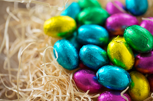 easter, confectionery and holidays concept - close up of chocolate eggs in foil wrappers in straw nest