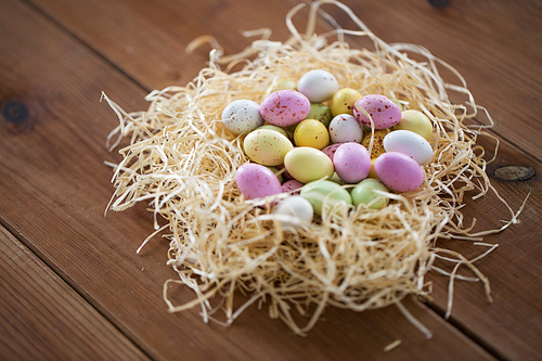 easter, confectionery and holidays concept - candy drop eggs in straw nest on wooden table
