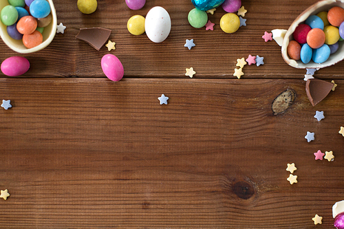 easter, sweets and confectionery concept - chocolate eggs and candy drops on wooden background