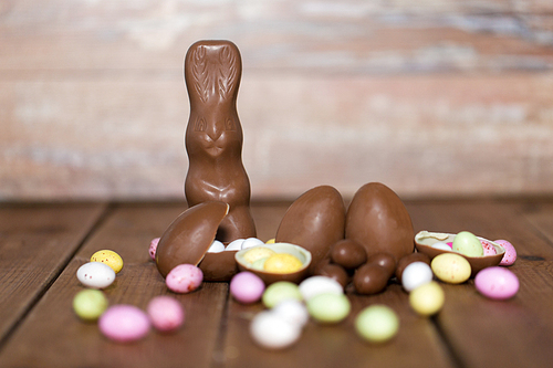 easter, sweets and confectionery concept - chocolate eggs, bunny and candy drops on wooden table