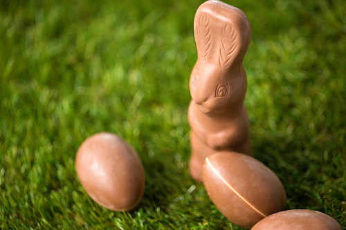 ., sweets and confectionery concept - close up of chocolate bunny and eggs on grass