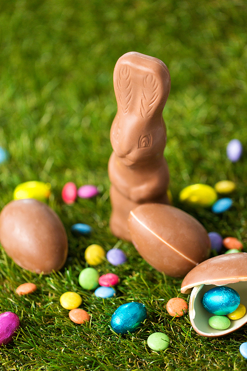 easter, sweets and confectionery concept - close up of chocolate bunny, eggs and candy drops on grass