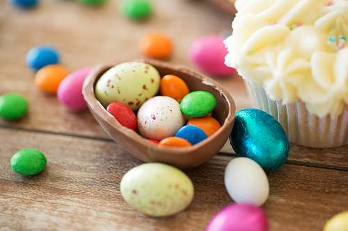 easter, food and holidays concept - close up of chocolate egg with candies and cupcake on wooden table