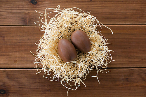 easter, confectionery and holidays concept - chocolate eggs in straw nest on wooden background