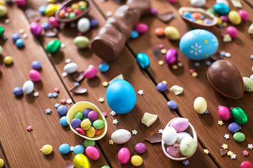 easter, sweets and confectionery concept - chocolate eggs, bunny and candy drops on wooden background