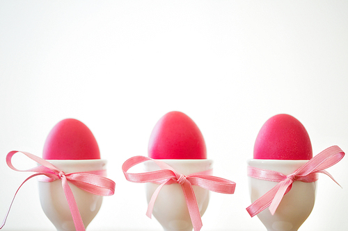 easter and holidays concept - pink colored eggs in ceramic cup holders with ribbon on white background