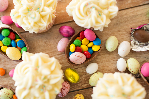 easter, food and holidays concept - close up of frosted cupcakes with chocolate eggs and candies on wooden table