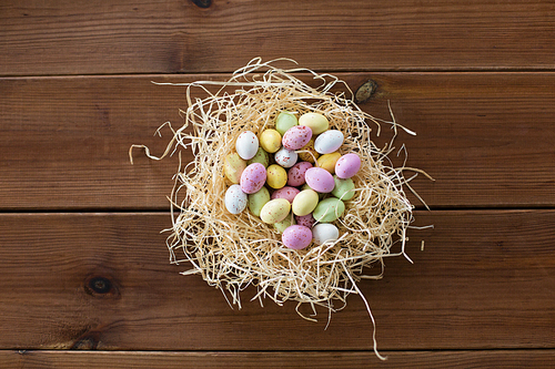 easter, confectionery and holidays concept - candy drop eggs in straw nest on wooden background