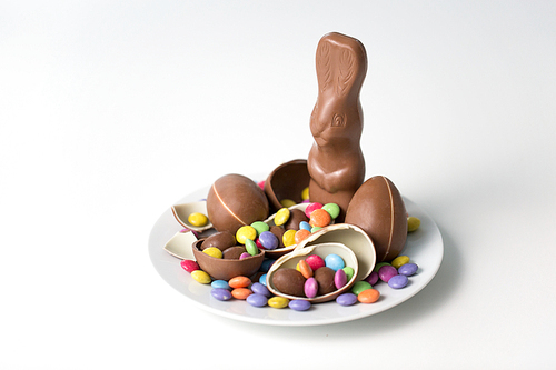 easter, sweets and confectionery concept - chocolate bunny, eggs and candy drops on white plate