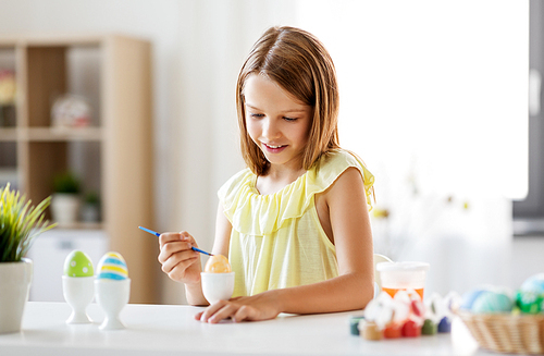 easter, holidays and people concept - happy girl coloring eggs with colors and brush at home