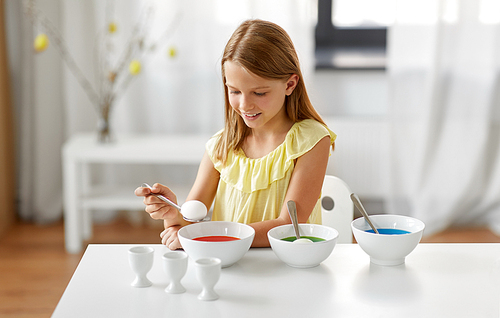 easter, holidays and people concept - happy girl coloring eggs by liquid dye at home