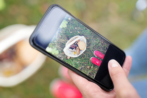 technology, nature and leisure concept - close up of woman photographing mushrooms in basket by smartphone in autumn forest