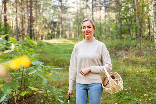 season and leisure people concept - young woman with wicker basket and knife picking mushrooms in forest