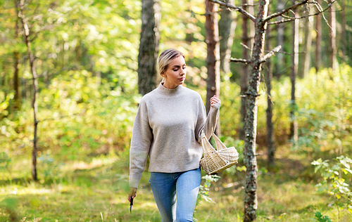 season and leisure people concept - young woman with wicker basket and knife picking mushrooms in forest