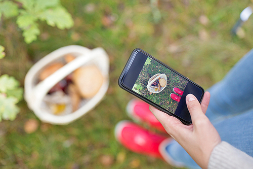 technology, nature and leisure concept - close up of woman photographing mushrooms in basket by smartphone in autumn forest