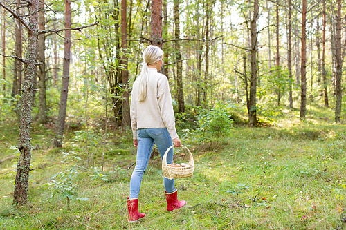 season, nature and leisure concept - young woman with mushrooms in basket walking along autumn forest