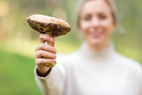 season, nature and leisure concept - close up of young woman holding mushroom in forest