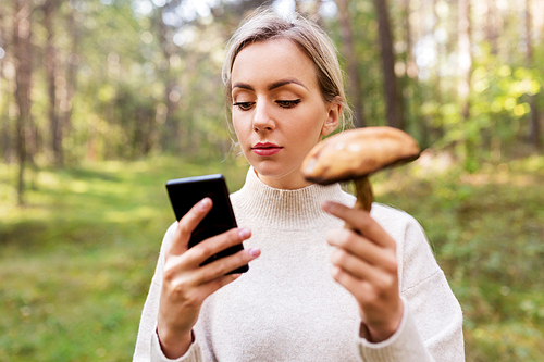 technology, people and leisure people concept - young woman with smartphone using app to identify mushroom in forest