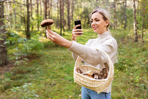 technology, people and leisure people concept - young woman with smartphone using app to identify mushroom in forest