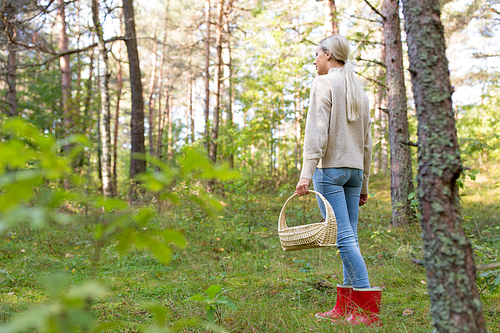 season, nature and leisure concept - young woman with mushrooms in basket walking along autumn forest