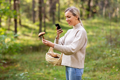 technology, people and leisure people concept - young woman with smartphone using app to identify mushroom in forest