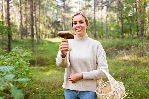 season and leisure people concept - young woman with basket and mushroom in autumn forest