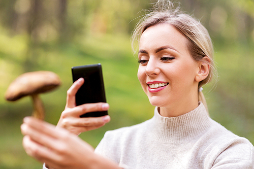 technology, people and leisure people concept - happy young woman with smartphone using app to identify mushroom in forest