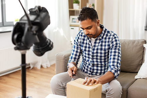 delivery, shipment and blogging concept - indian male . opening parcel box and recording video by camera at home