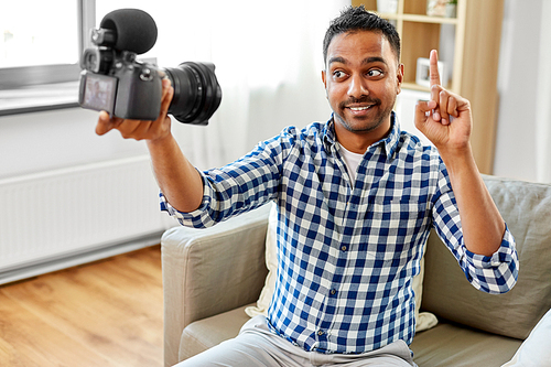 blogging, videoblog and people concept - smiling indian male video . with camera videoblogging pointing finger up at home