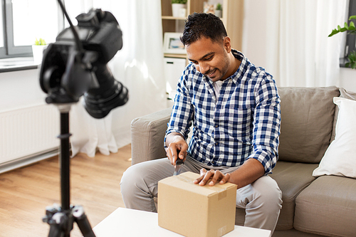 delivery, shipment and blogging concept - happy indian male . opening parcel box and recording video by camera at home