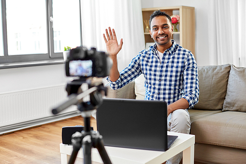 blogging, videoblog and people concept - smiling indian male . with camera recording video and waving hand at home office