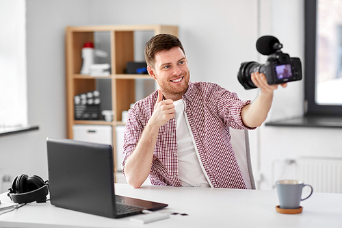 blogging, videoblog and people concept - male . holding camera, recording video blog and showing thumbs up at home office
