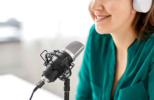 technology, mass media and people concept - close up of woman with microphone and headphones talking and recording podcast at studio