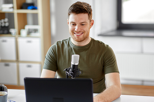 technology, mass media and podcast concept - happy young male audio . with laptop computer and microphone broadcasting at home office
