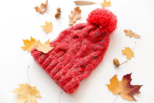 season, headwear and clothes concept - knitted woollen hat and fallen autumn leaves on white background