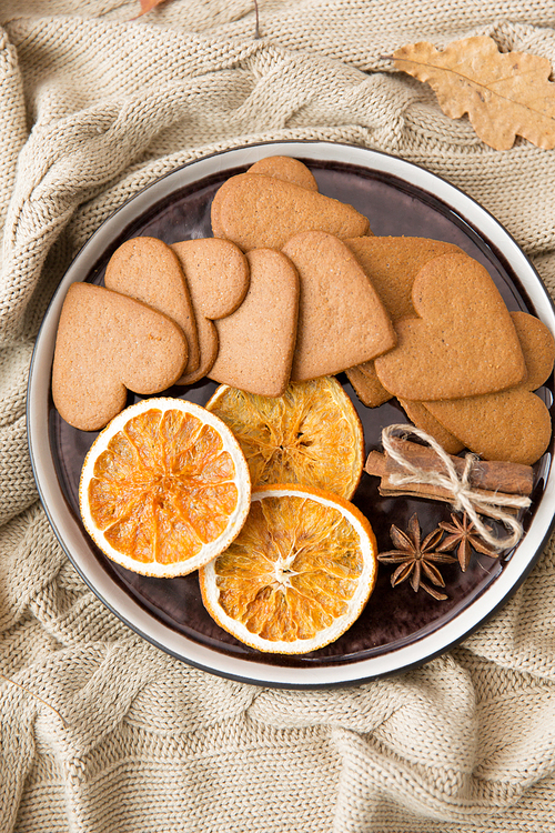 drinks and season concept - plate with heart shaped gingerbread cookies, dried oranges, cinnamon and anise on warm blanket
